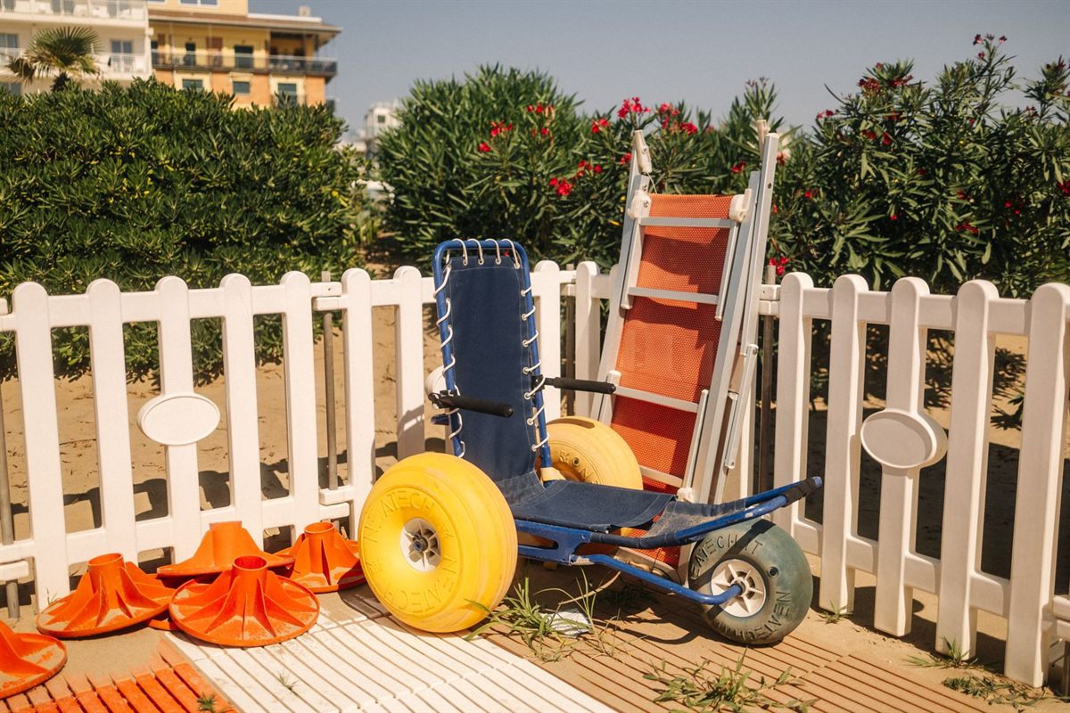 A beach wheelchair with balloon wheels beside a white fence at the beach