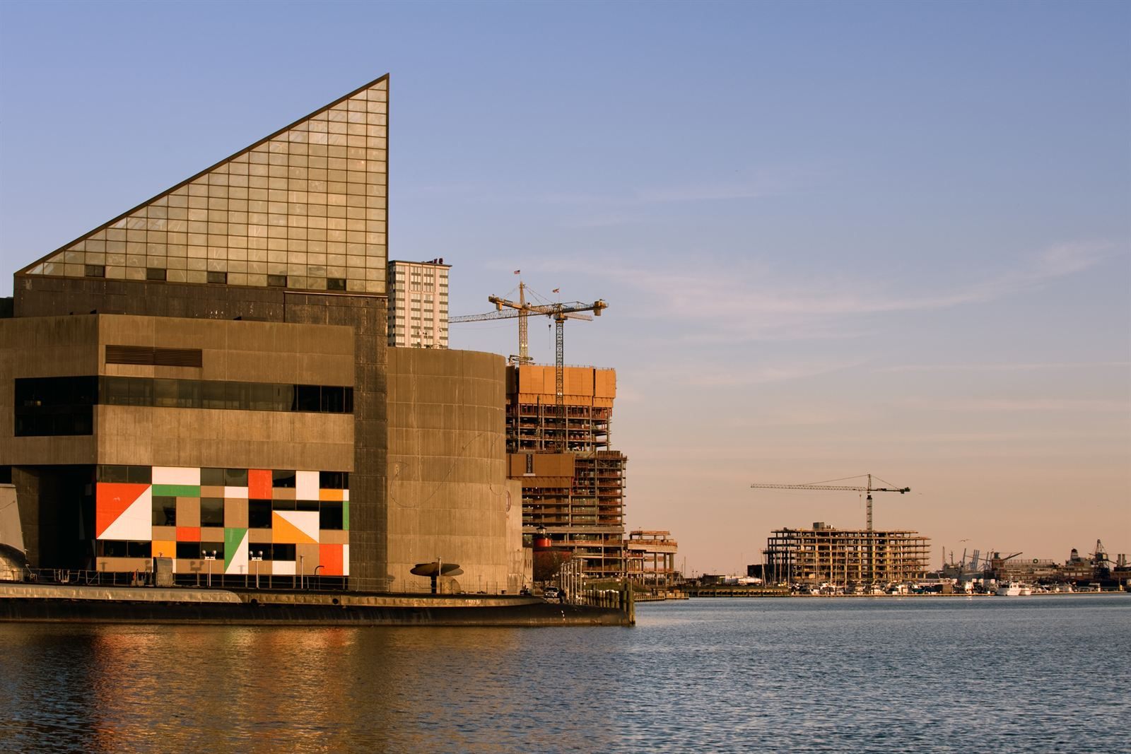 The glass-peaked National Aquarium building on Baltimore's Inner Harbor at sunset, with cranes beyond