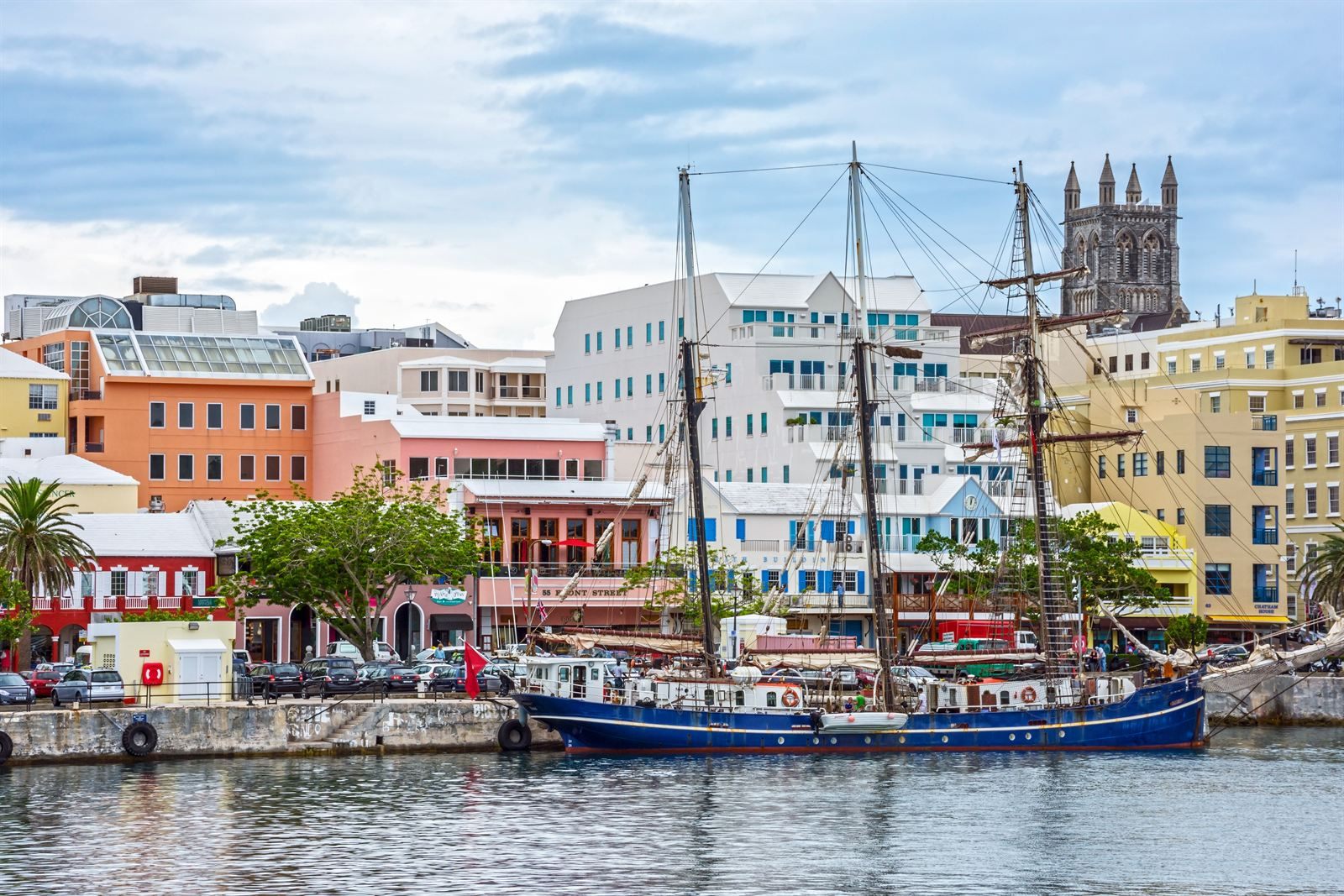 Tall ship moored in front of pastel waterfront buildings and a church tower in Hamilton, Bermuda