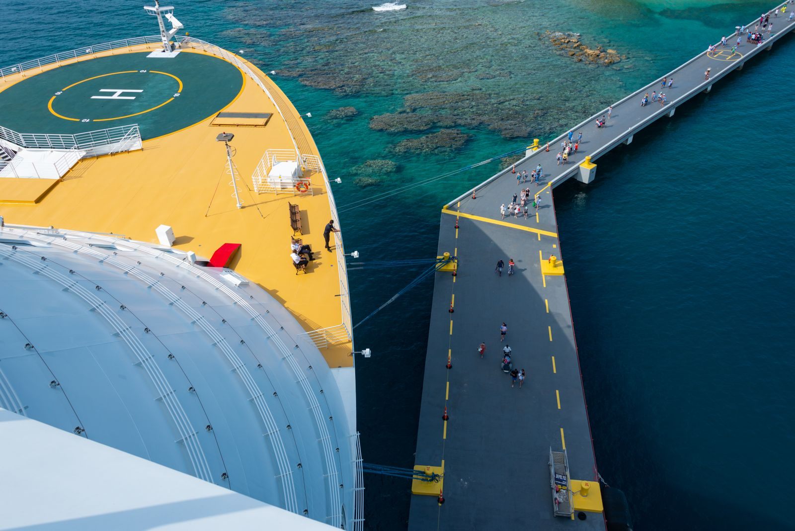 Aerial view of a cruise ship bow beside a long pier over clear blue water, where people decide what to do at cruise ports
