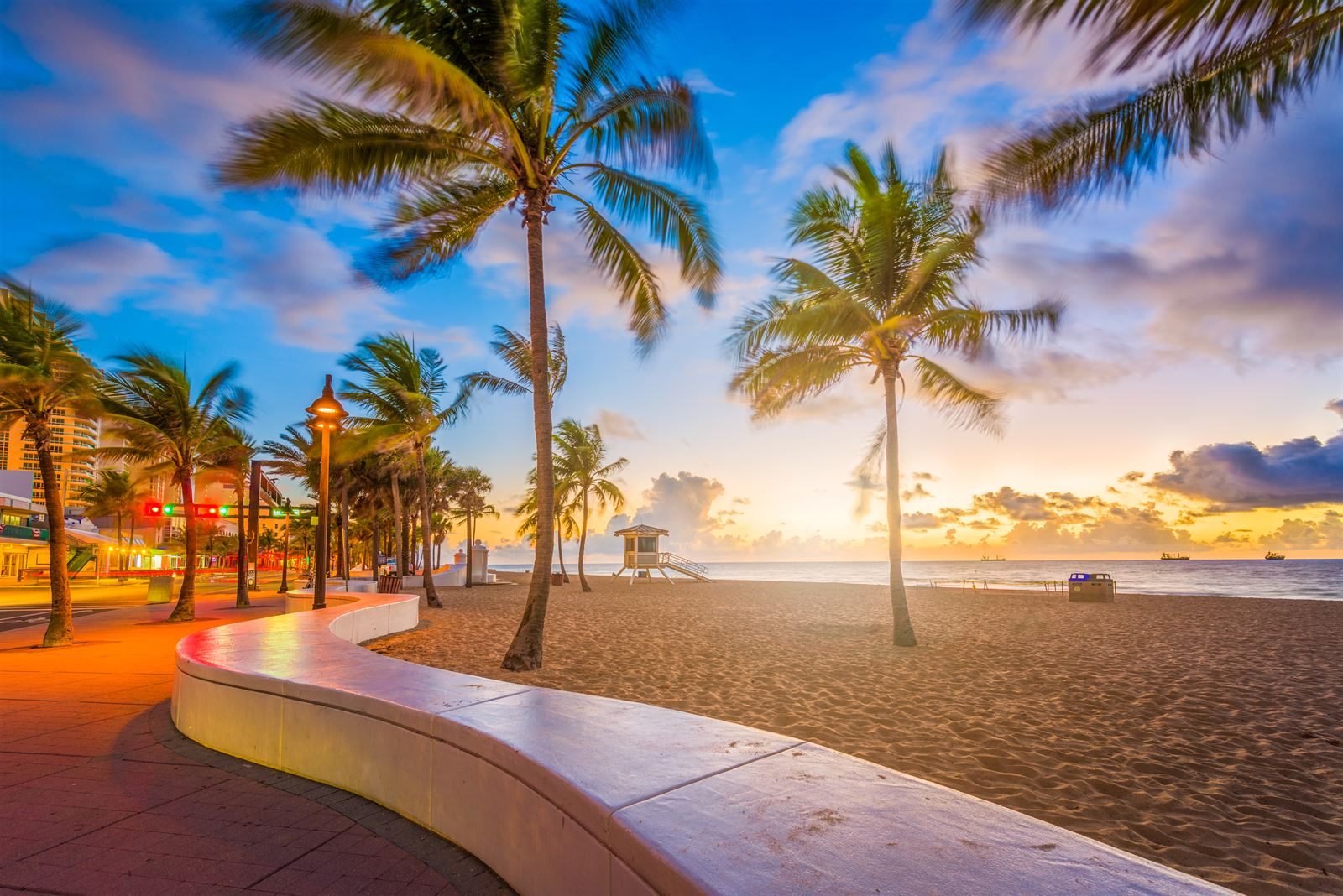 Palm trees, a curving beach wall and a lifeguard stand on Fort Lauderdale beach at sunrise