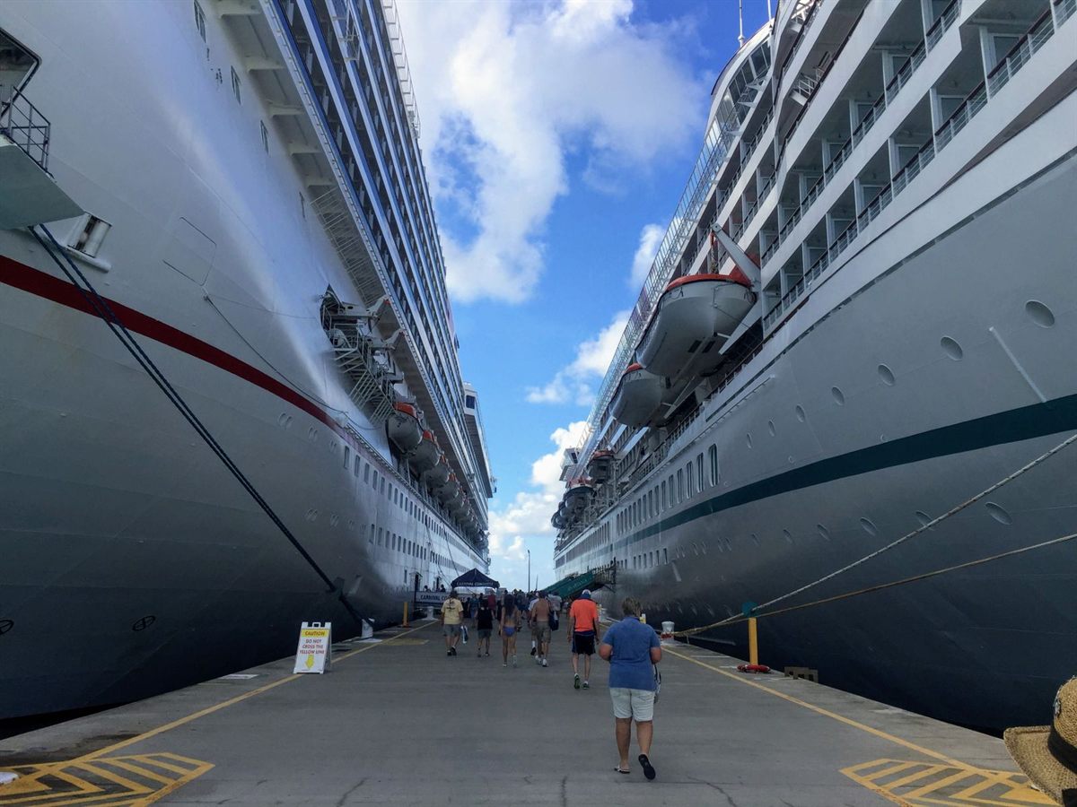 Passengers walking on a pier between two large cruise ships