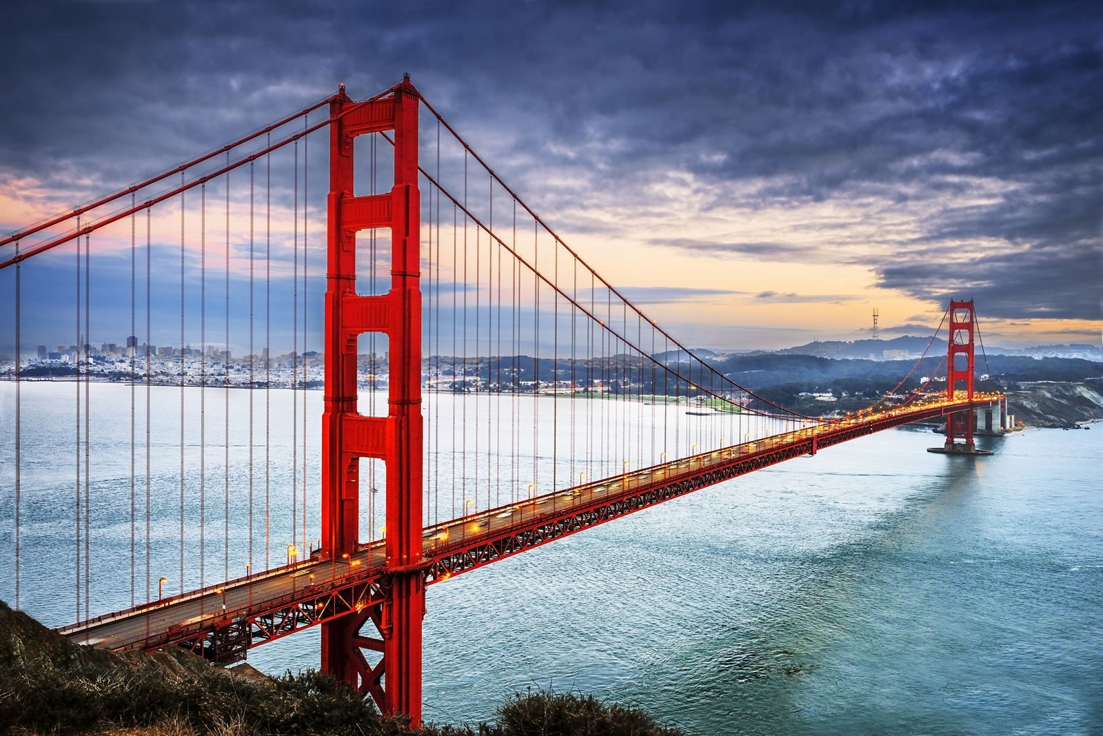 The Golden Gate Bridge spanning the bay with the San Francisco skyline in the distance under evening clouds