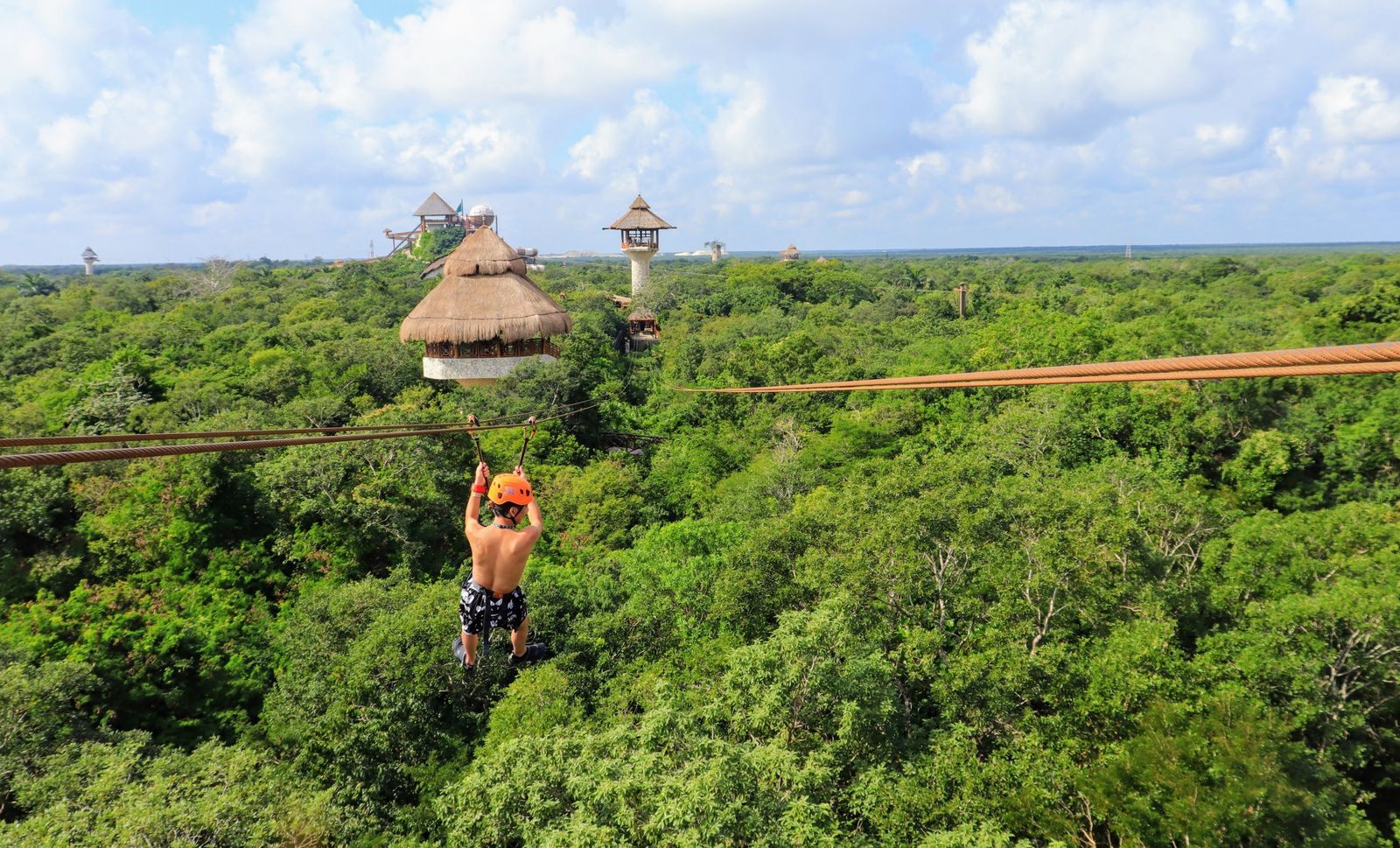 A zip-liner flying over green forest towards a thatched tower, one of the adventure types of shore excursions