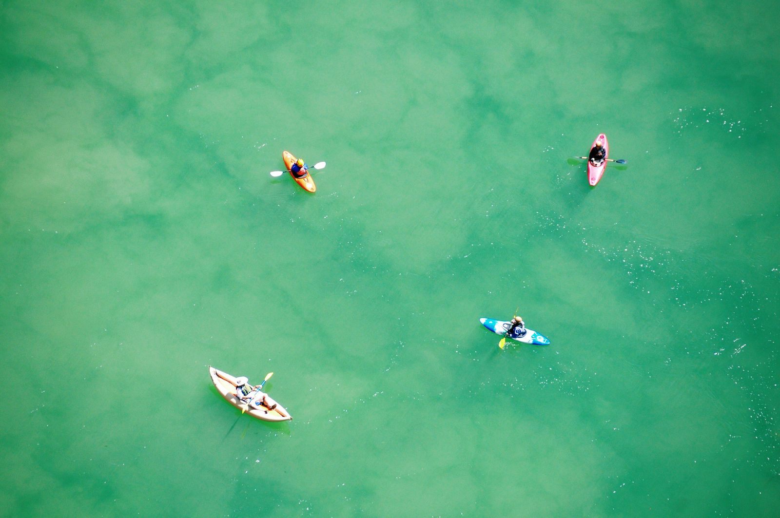 Aerial view of four kayakers on turquoise water, a beach and water port activity